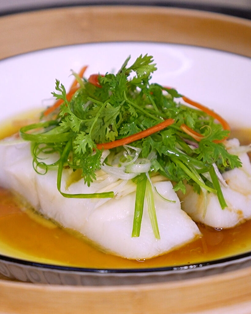 close-up of tender steamed fish with fragrant oil and herbs in steam basket
