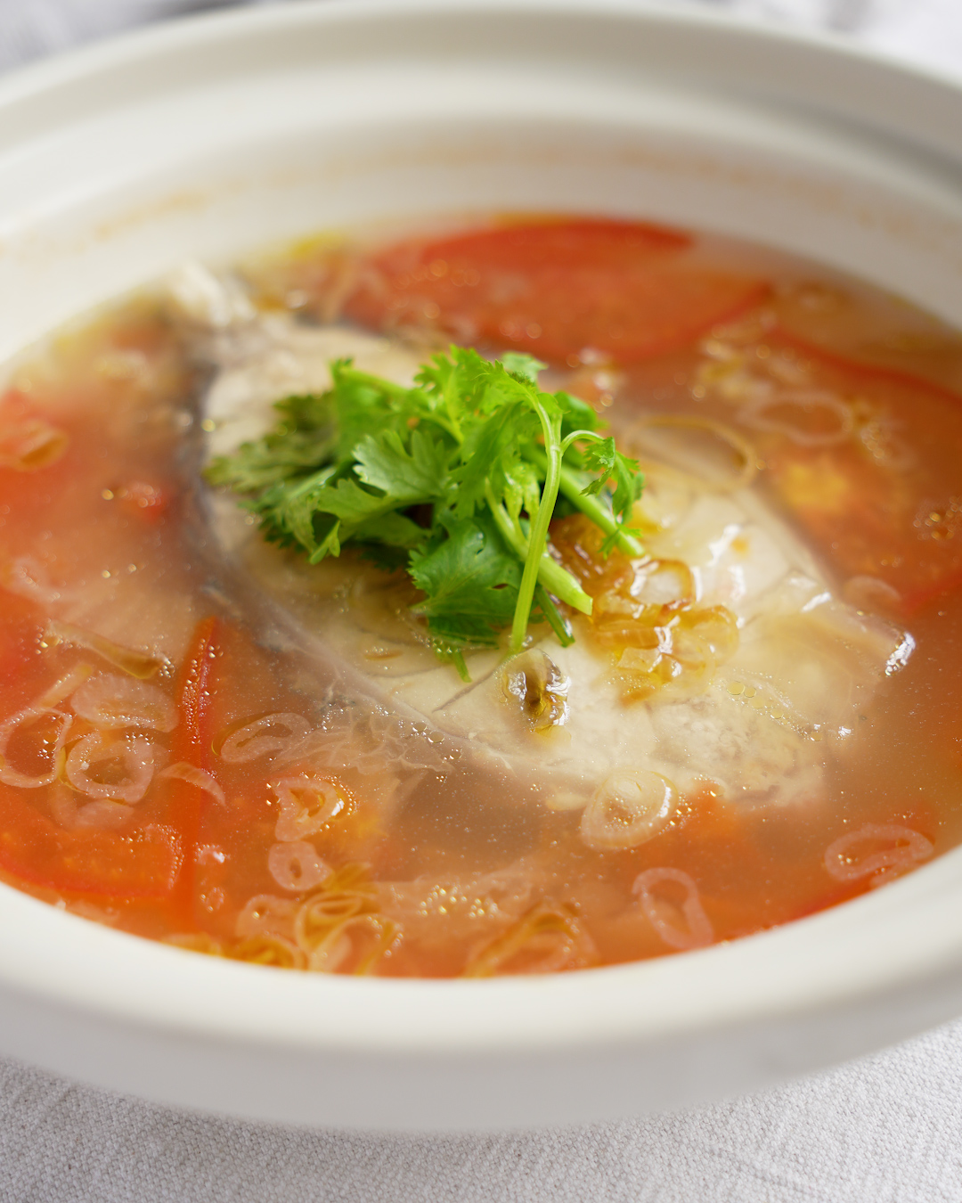 Chinese fish soup with tomato and Tianjin preserved vegetables cooking in a ceramic pot