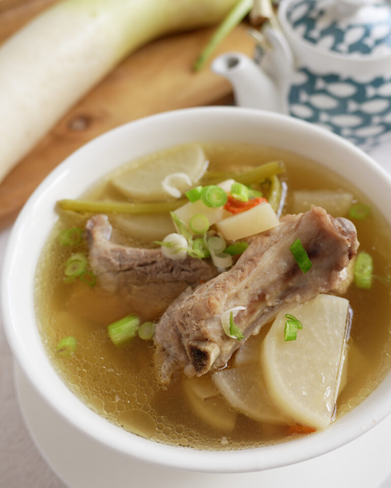 Pork ribs soup with radish and goji berries in a bowl, garnished with spring onions