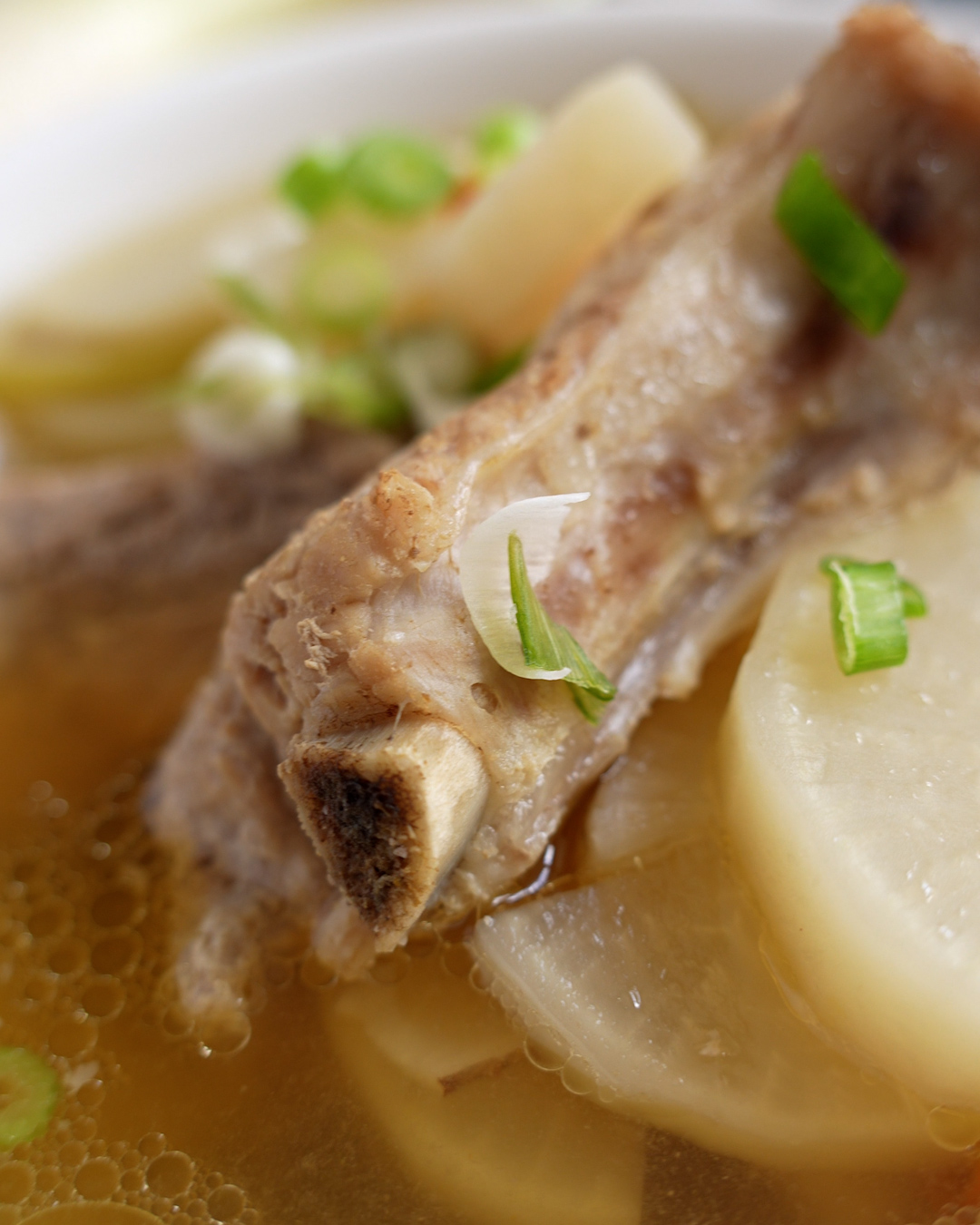 Bowl of pork ribs soup with radish, goji berries and yuk chuk, topped with spring onions