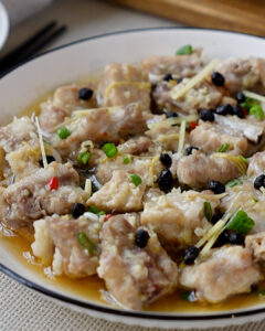 Steamed pork ribs with fermented black beans on a plate, garnished with spring onions