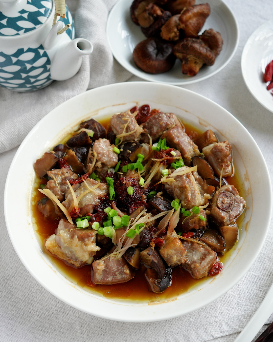 Steamed pork ribs with mushrooms and goji berries on a plate, garnished with spring onion