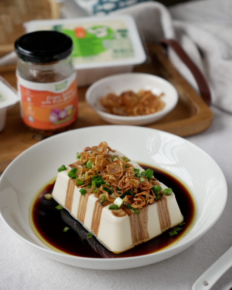 Steamed tofu with shallot oil served on a white plate, garnished with spring onion and crispy shallots