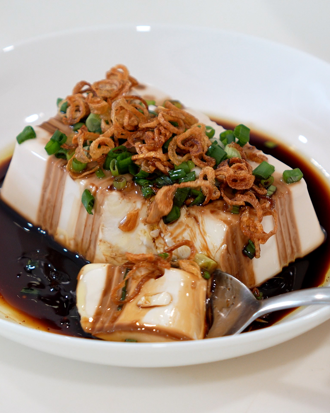 Overhead shot of steamed tofu with shallot oil, crispy shallots and chopped spring onion