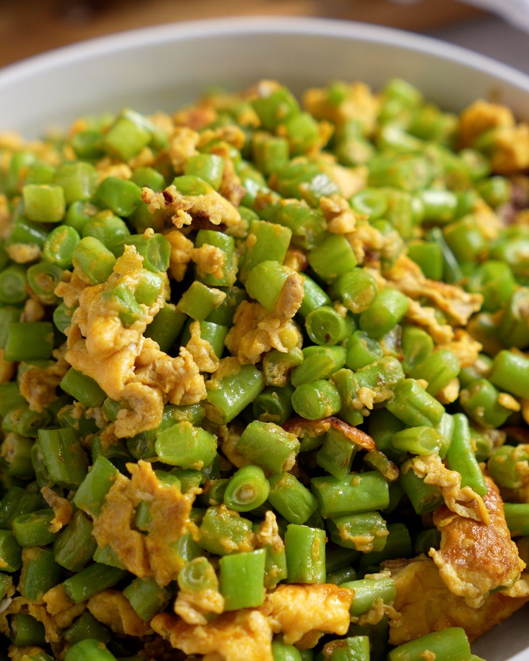 Close-up of diced french beans and scrambled egg tossed together in a stir fry
