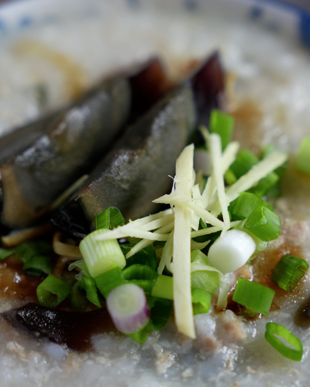 Stirring century egg pieces into minced pork porridge cooked in a rice cooker