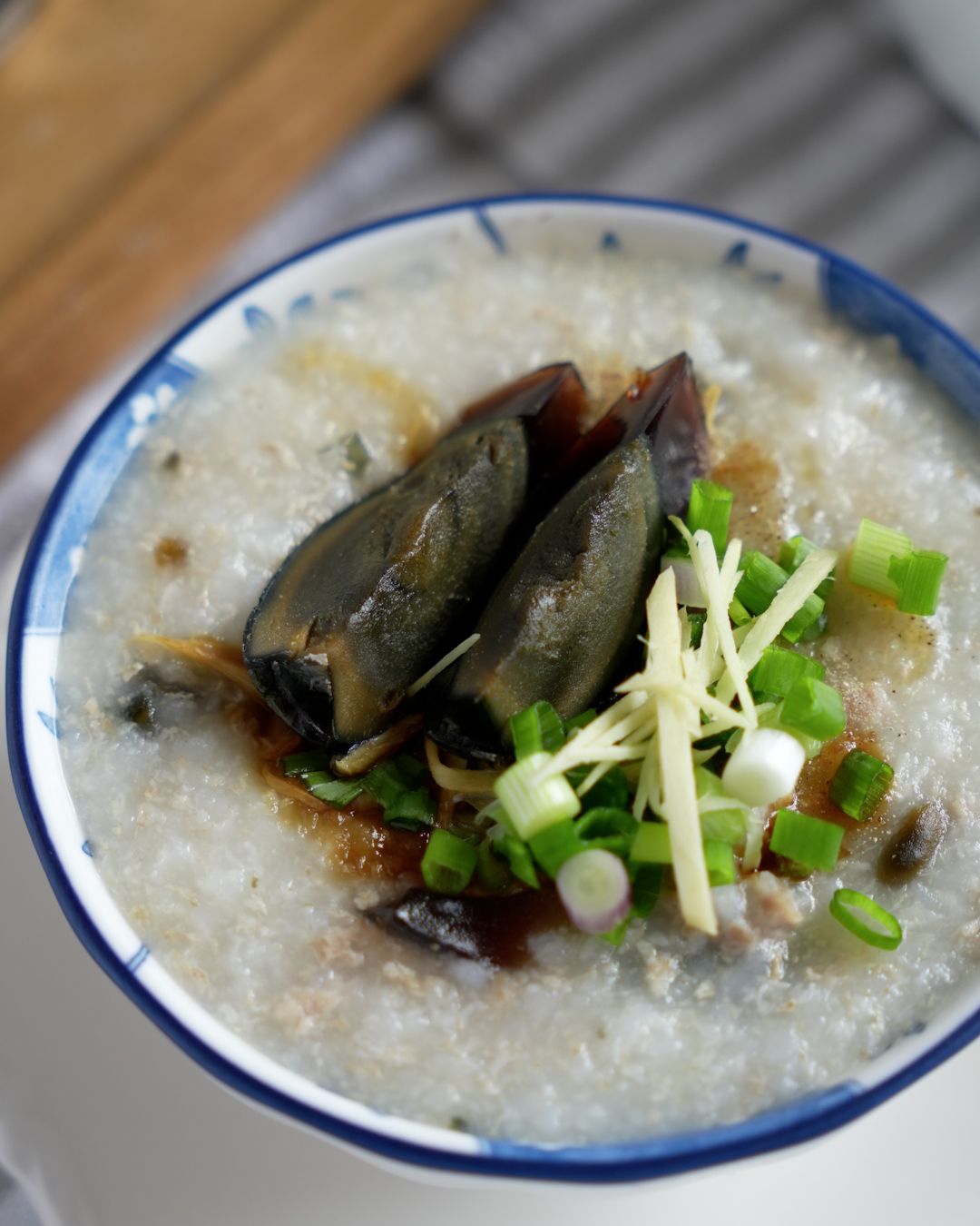 Bowl of minced pork century egg porridge topped with sesame oil, light soy sauce, and julienned ginger