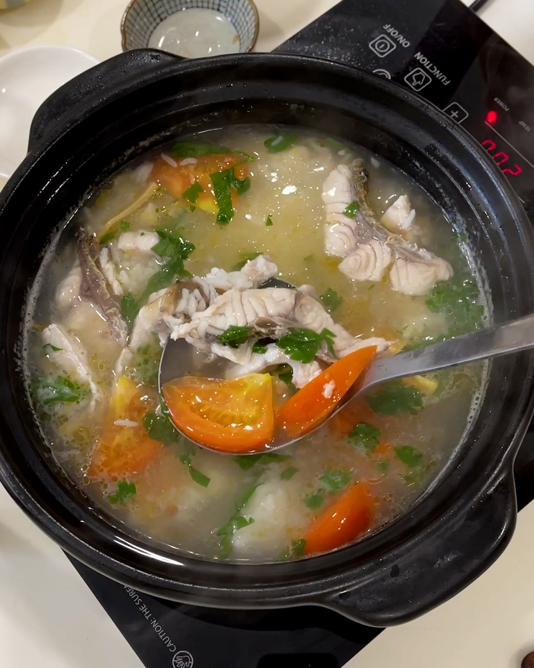 Overhead view of sour plum fish soup with leftover rice, fish slices and tomato