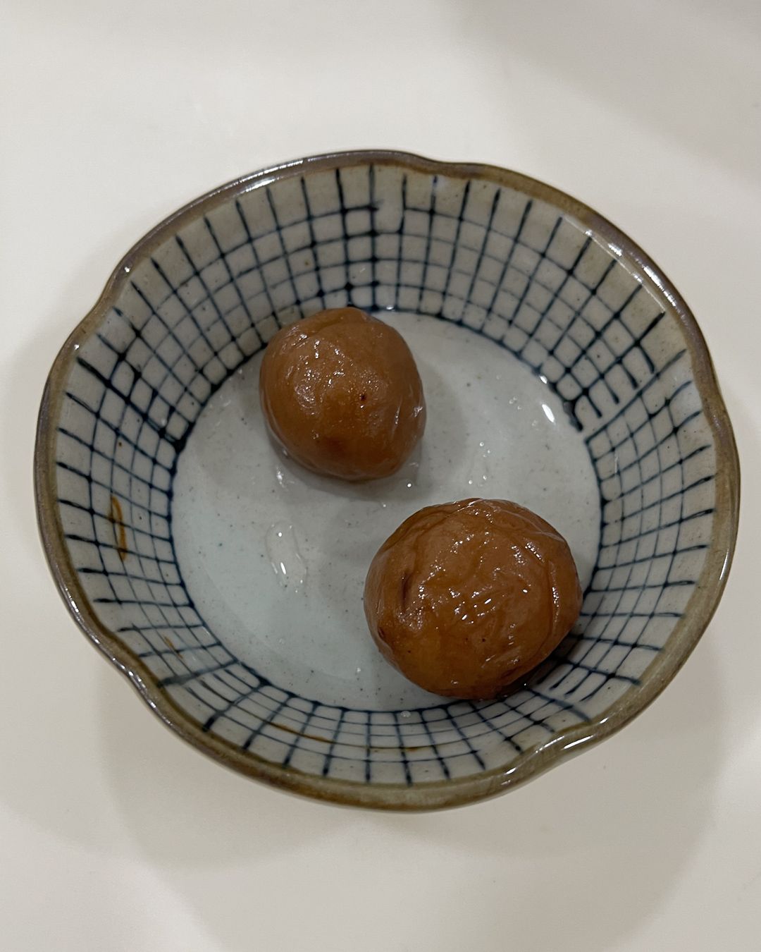 Two salted water plums (sour plum) in a small dish
