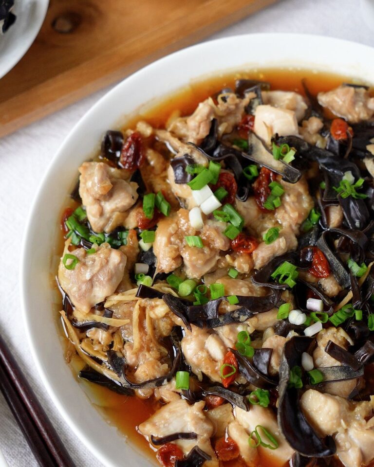 Overhead close-up of steamed chicken with black fungus, goji berries, and spring onion in a white bowl