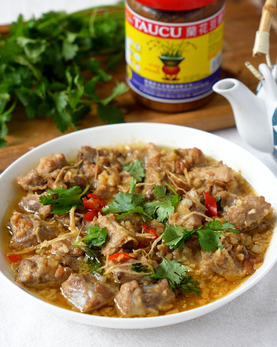 Steamed pork ribs with taucu fermented bean paste garnished with coriander next to a jar of taucu