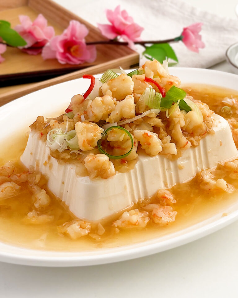 Steamed tofu with preserved radish and prawns topped with spring onion and chilli on a white plate