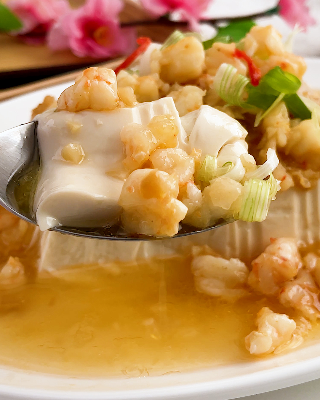 Spoonful of steamed tofu with preserved radish and prawns lifted from the plate showing the silky tofu texture
