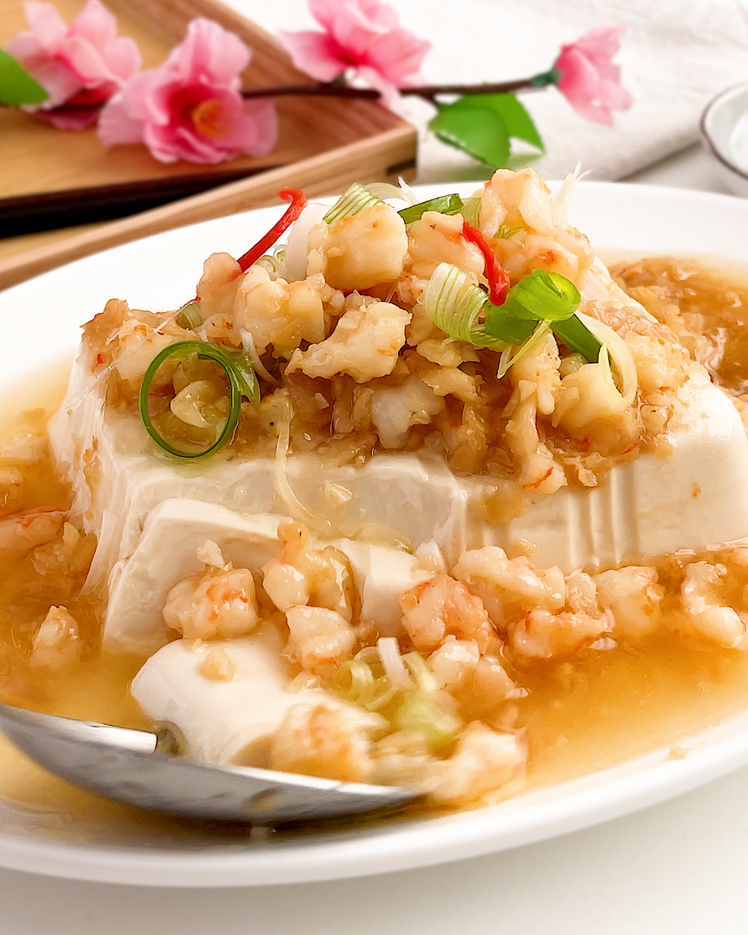 Close-up of steamed tofu with preserved radish and prawns sauce, garnished with spring onion and chilli
