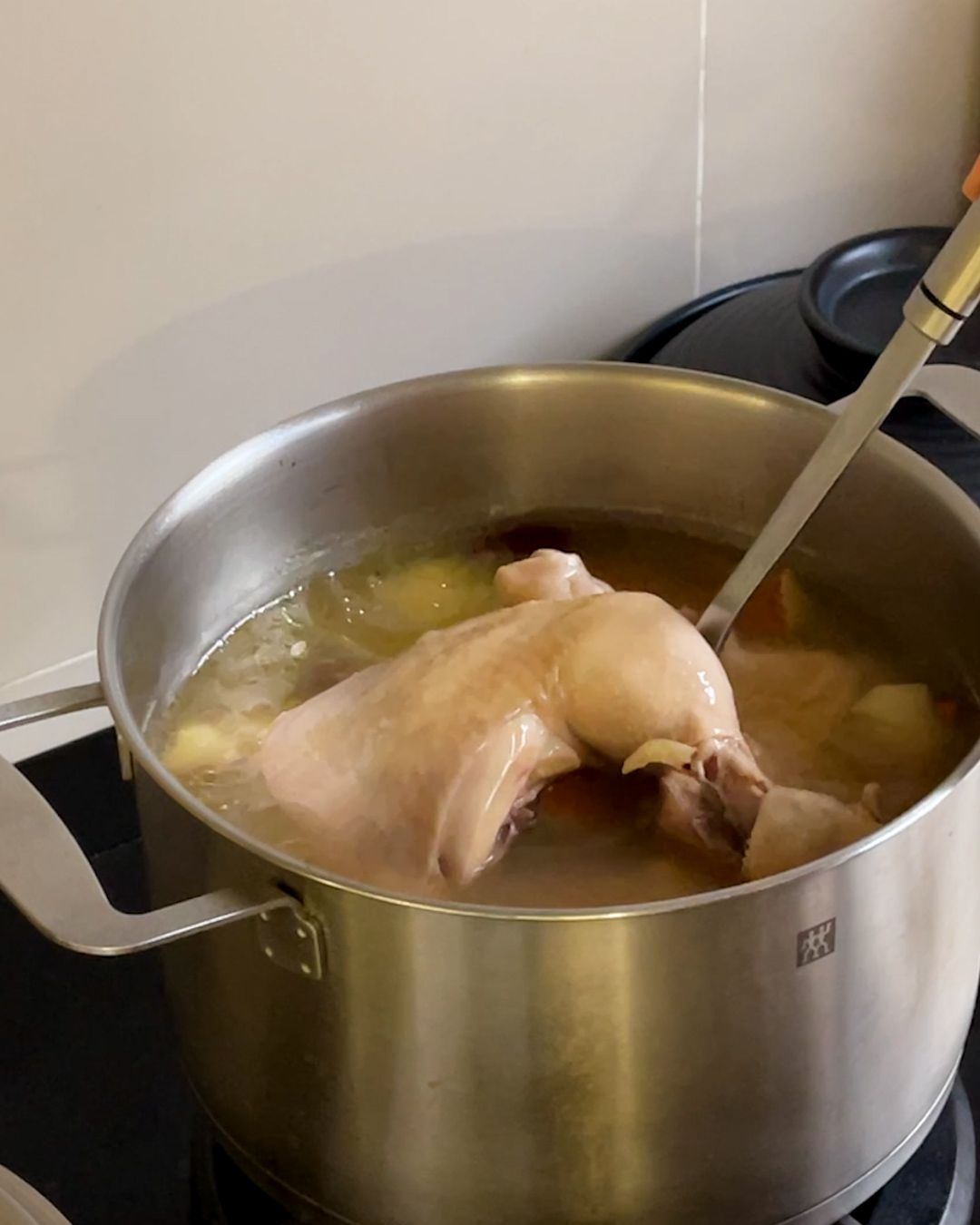 Old cucumber soup with chicken simmering in a stainless steel pot with a whole chicken leg and old cucumber chunks