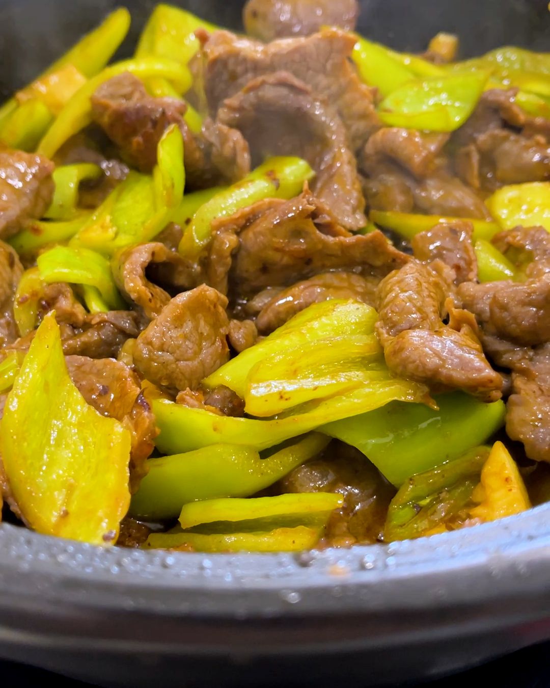 Close-up of beef and green pepper stir fry in a pan, with thin slices of beef and green chili pepper pieces in a glossy black bean sauce