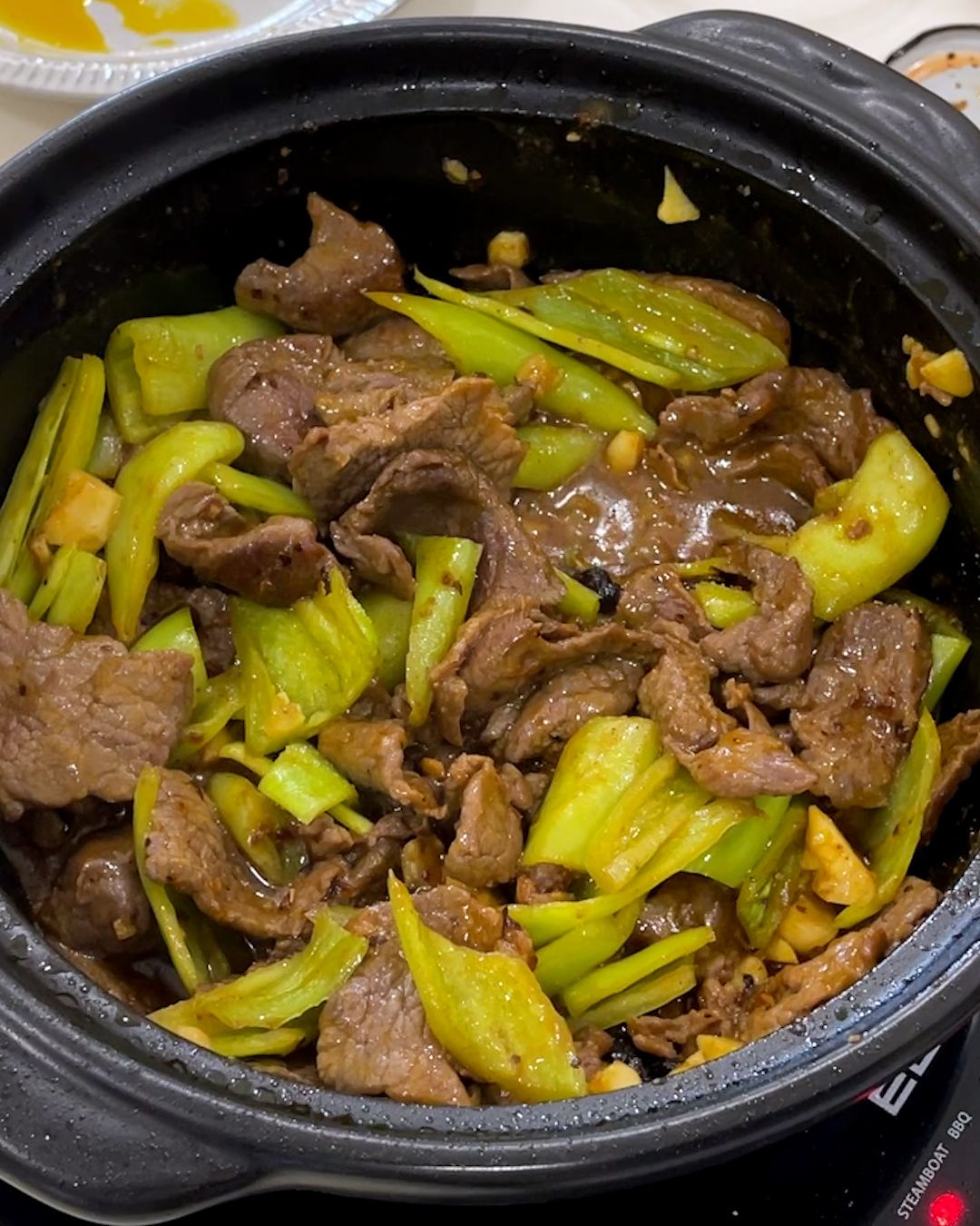 Finished beef and green pepper stir fry in a black claypot, showing seared beef slices, green chili peppers and chopped garlic