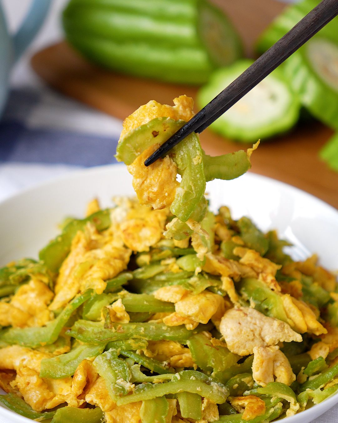 Bitter gourd stir fry with egg lifted with chopsticks from a white bowl