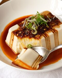 Cold silken tofu with chili oil and soy sauce in a white bowl, topped with spring onion