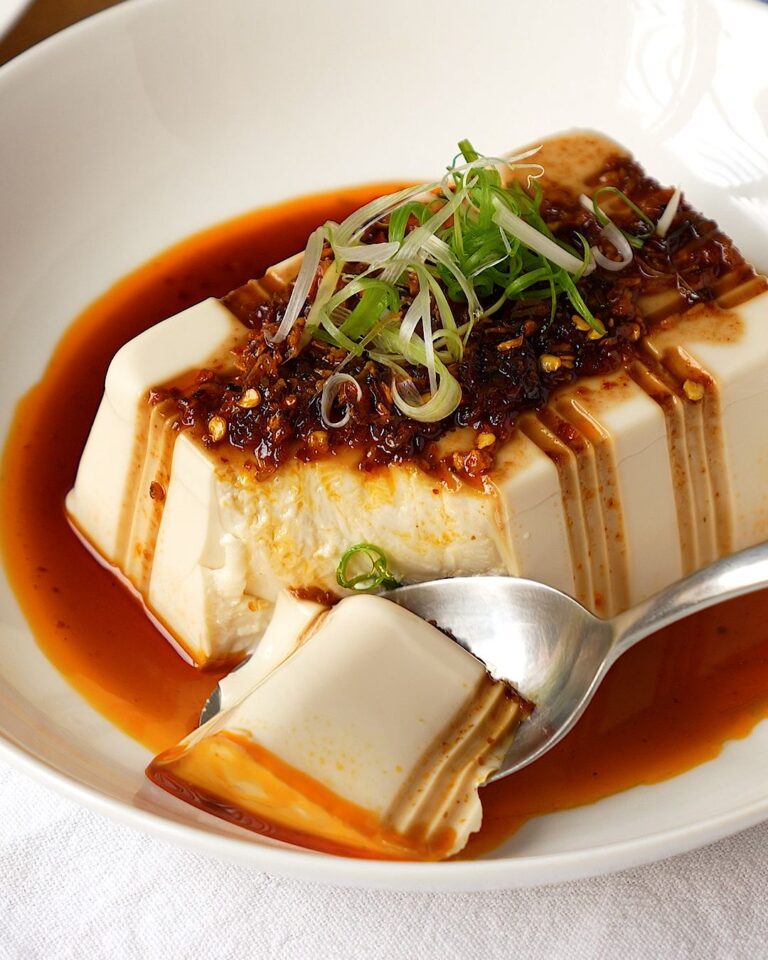 Cold silken tofu with chili oil and soy sauce in a white bowl, topped with spring onion