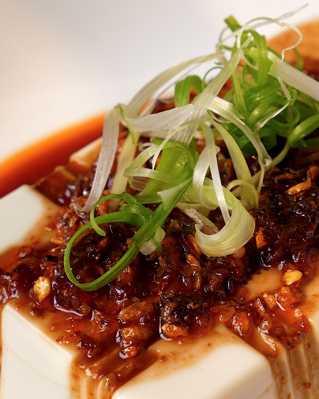 Close up of chili oil and spring onion on top of cold silken tofu