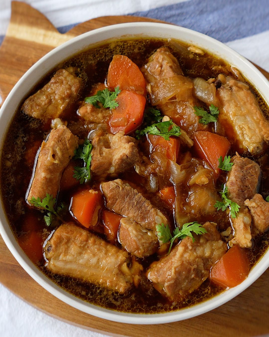 Chinese pork rib stew with carrots and onions in a white bowl, garnished with coriander