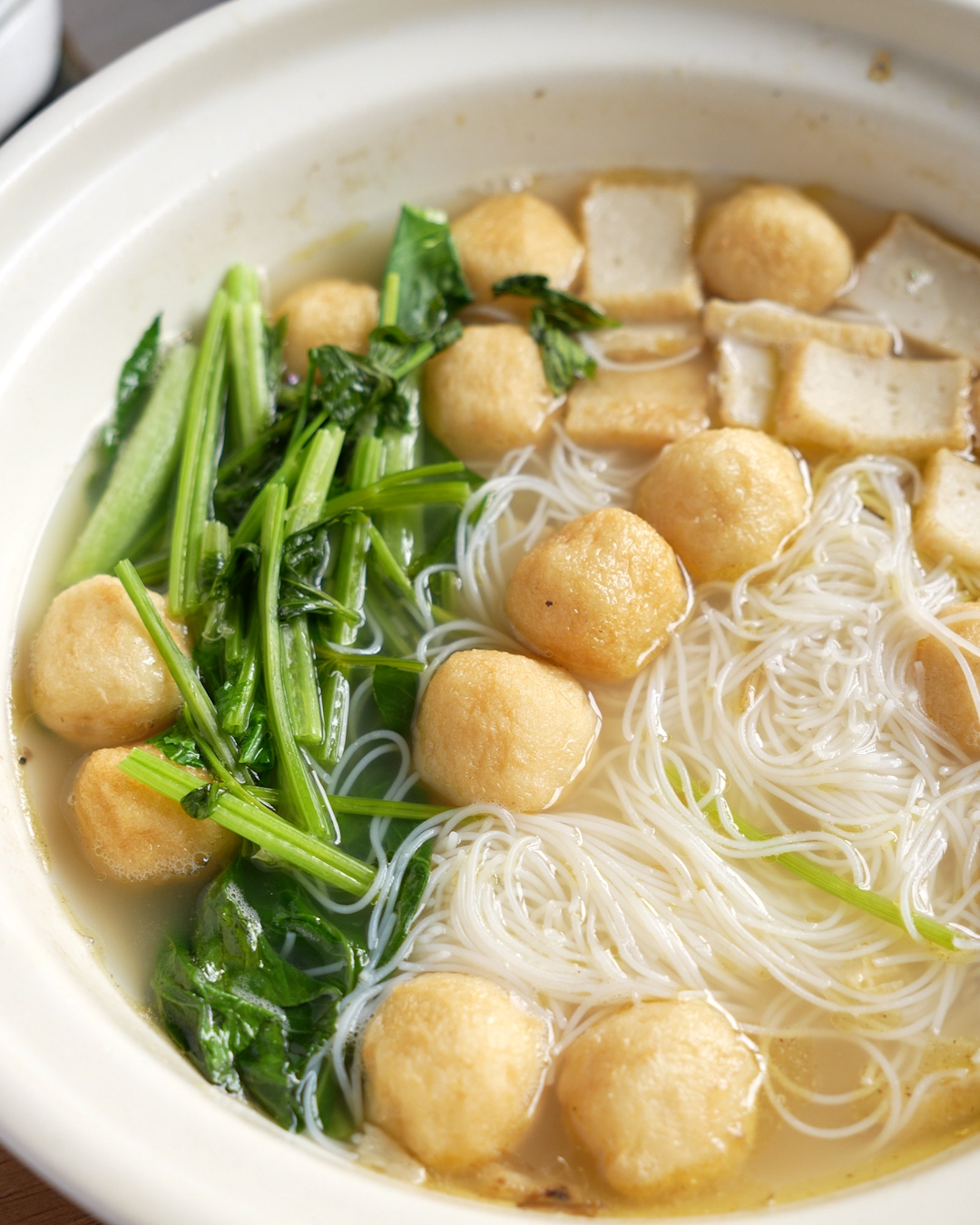 Close-up of homestyle fish ball noodle soup with bouncy fish balls, sliced fish cake, rice vermicelli and greens in clear broth