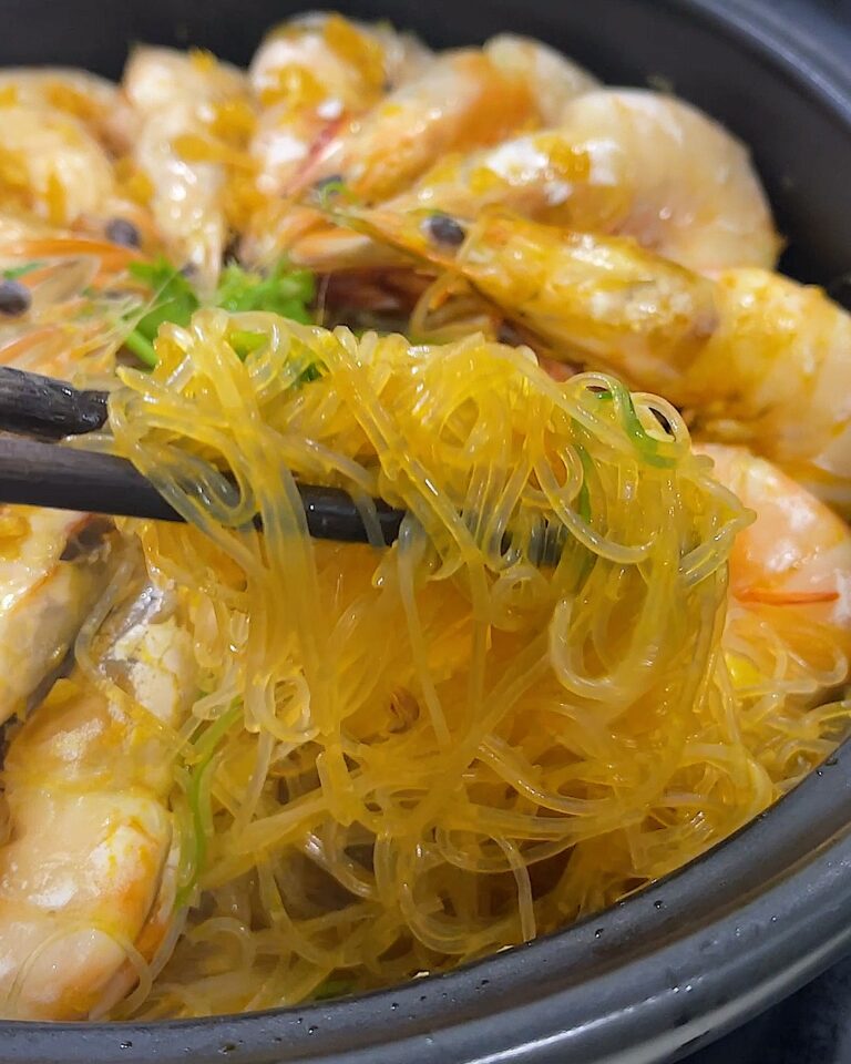 Chopsticks lifting garlic prawn glass noodles from a black pot of prawns cooked in garlic oil