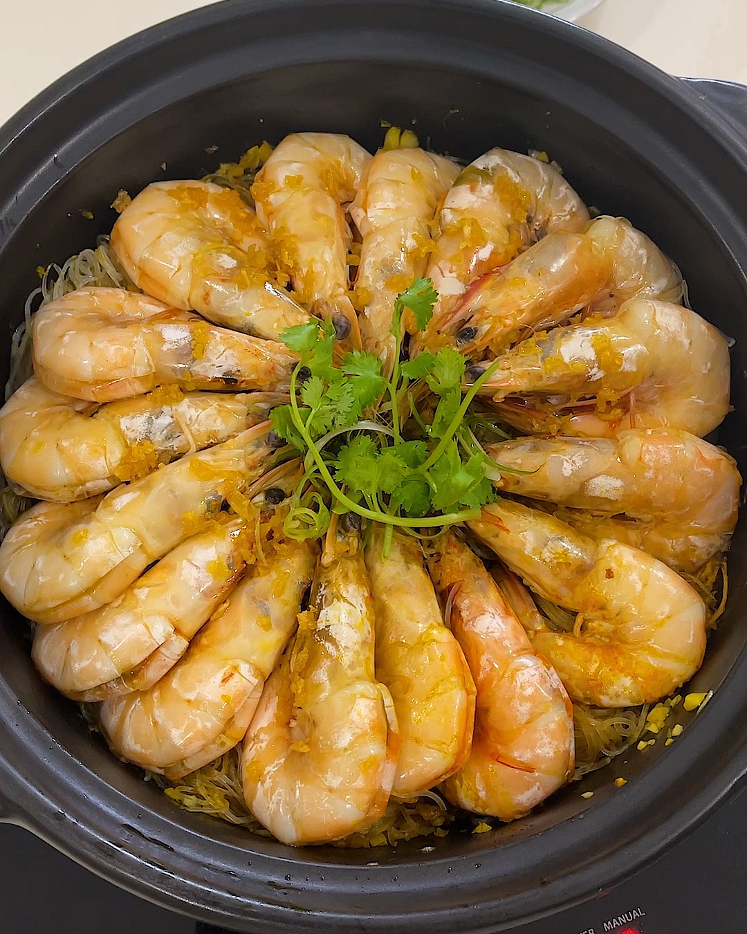 Overhead view of garlic prawn glass noodles in a black pot, with prawns arranged in a circle and coriander in the centre
